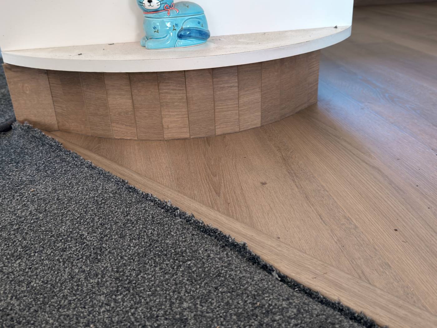 Oak-look planks laid up to the carpet, with the curved bench base clad in matching planks
